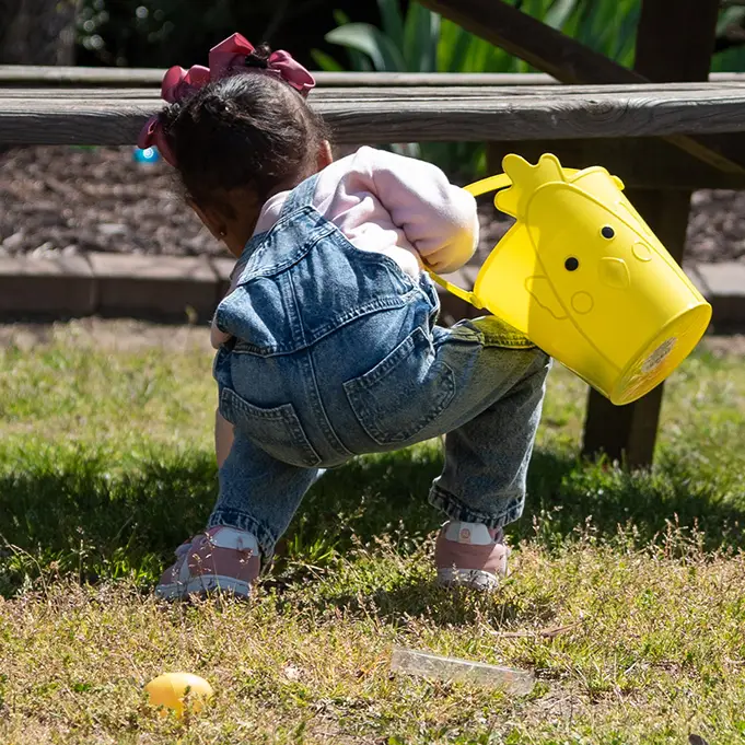 Child in overalls holding a bucket and collecting plastic eggs